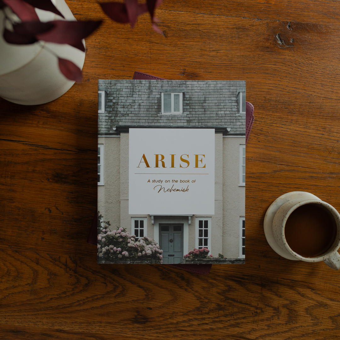Book titled 'Arise' on a wooden table with a cup of coffee and flowers.