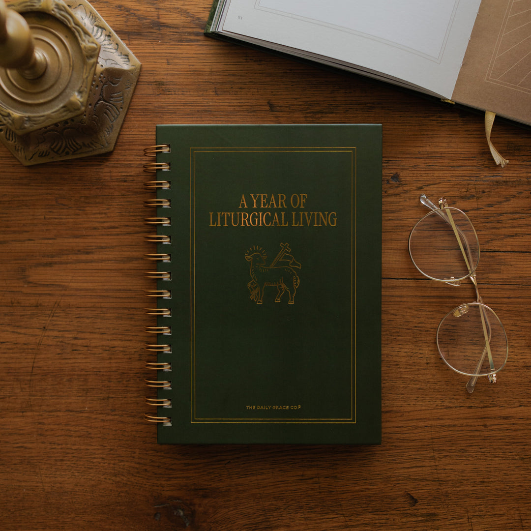 A Year of Liturgical Living on a wooden table next to a pair of glasses and a bronze colored candlestick