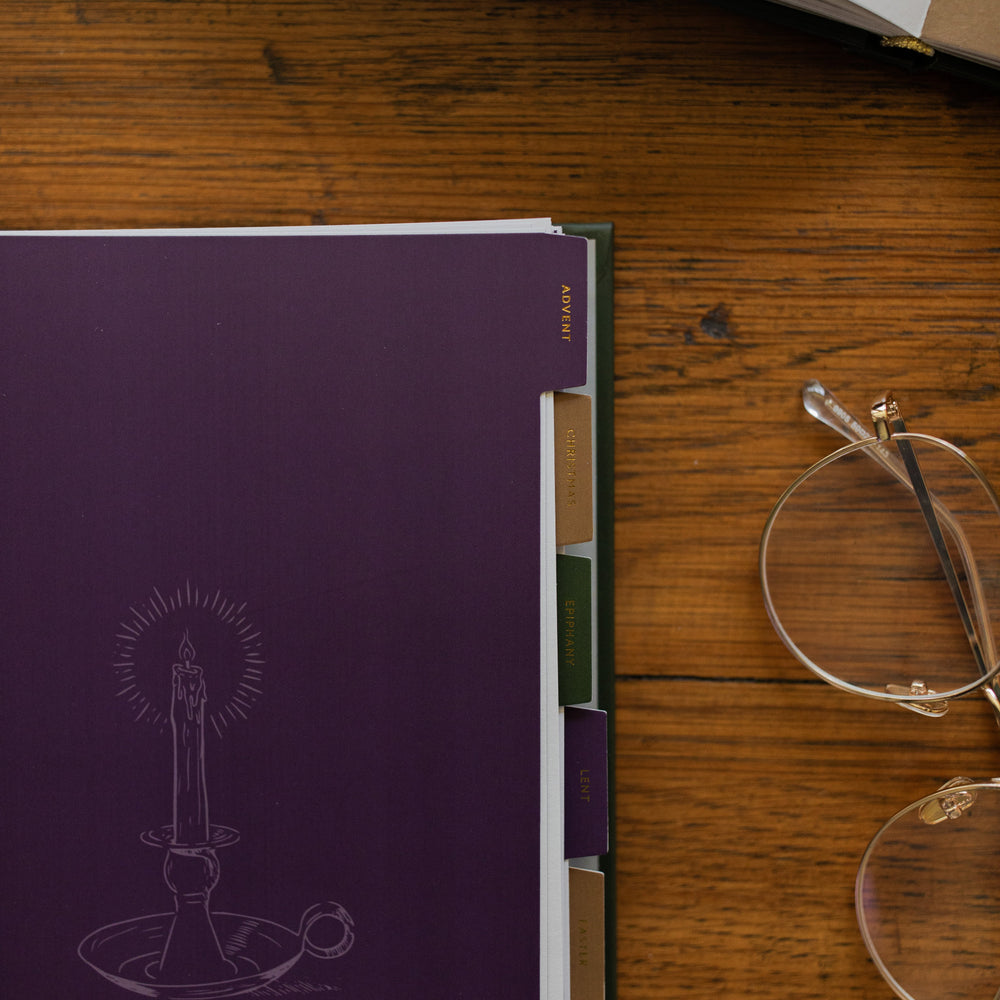 A Year of Liturgical Living up close to the Advent section on a wooden table next to a pair of glasses