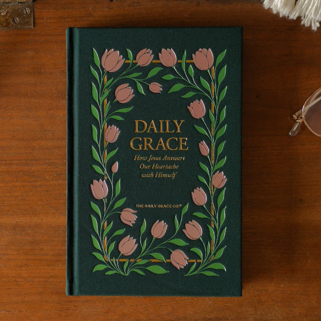 The Daily Grace Hardcover book cover on a wooden desk near a pair of glasses