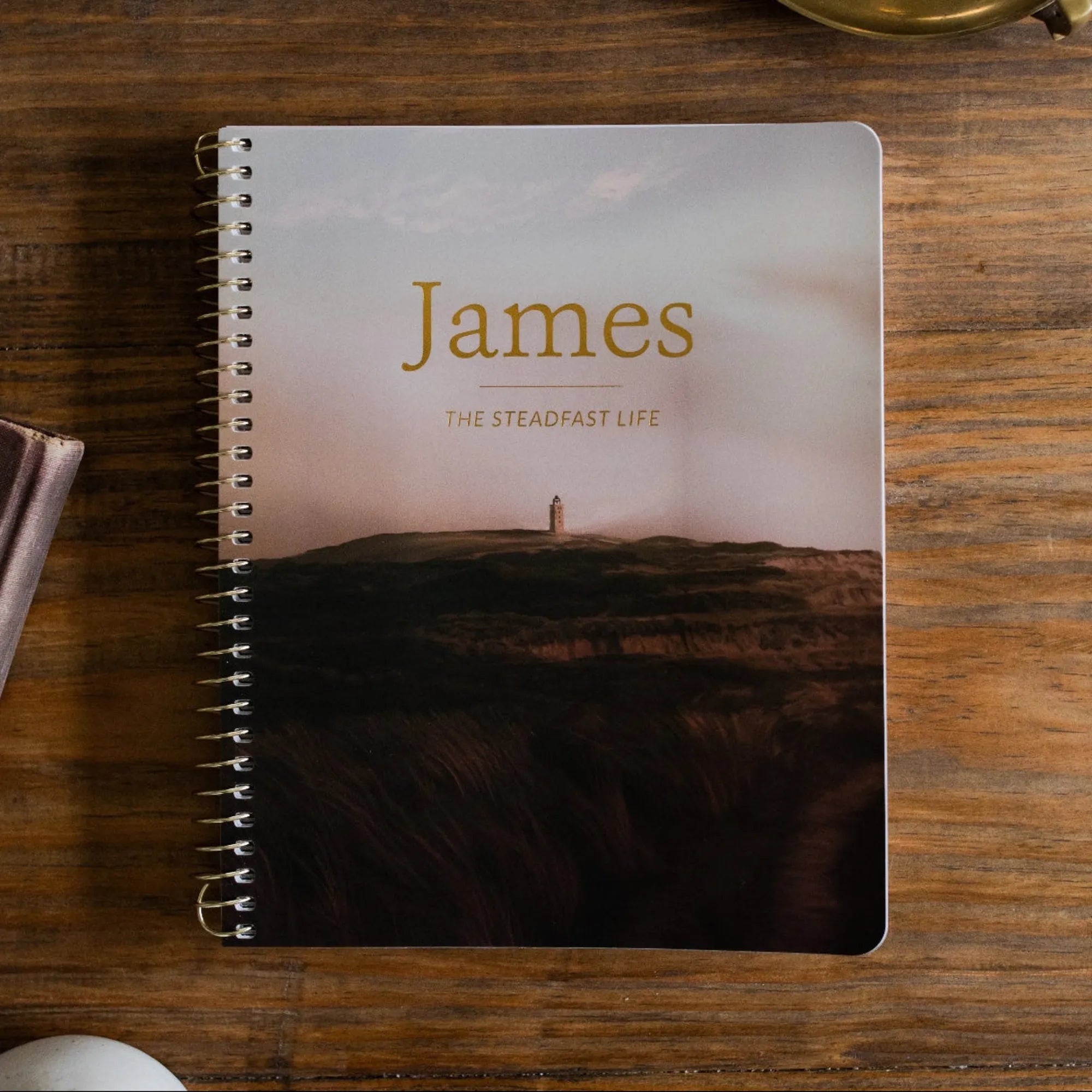 James Men's Spiral study Cover on a wooden table next to a bronze oil lamp