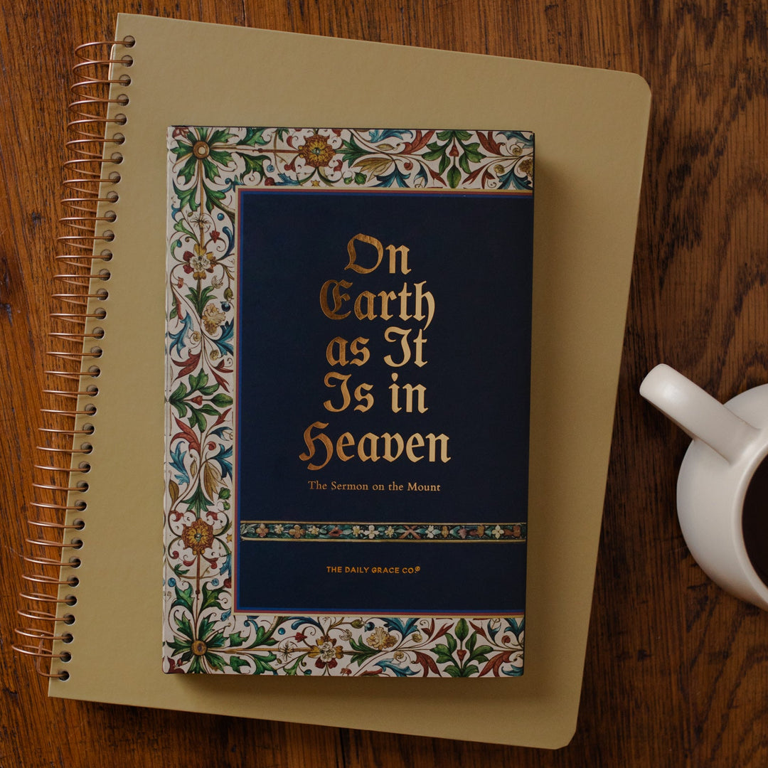 Book titled 'On Earth as It Is in Heaven' on a wooden surface with a cup of coffee.