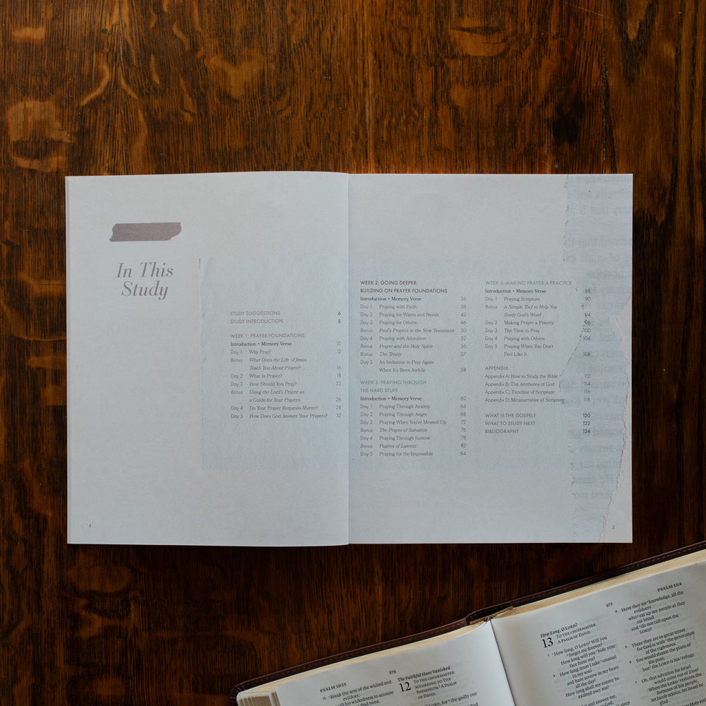 The Pray Study opened to the table of contents page on a wooden table near an open bible