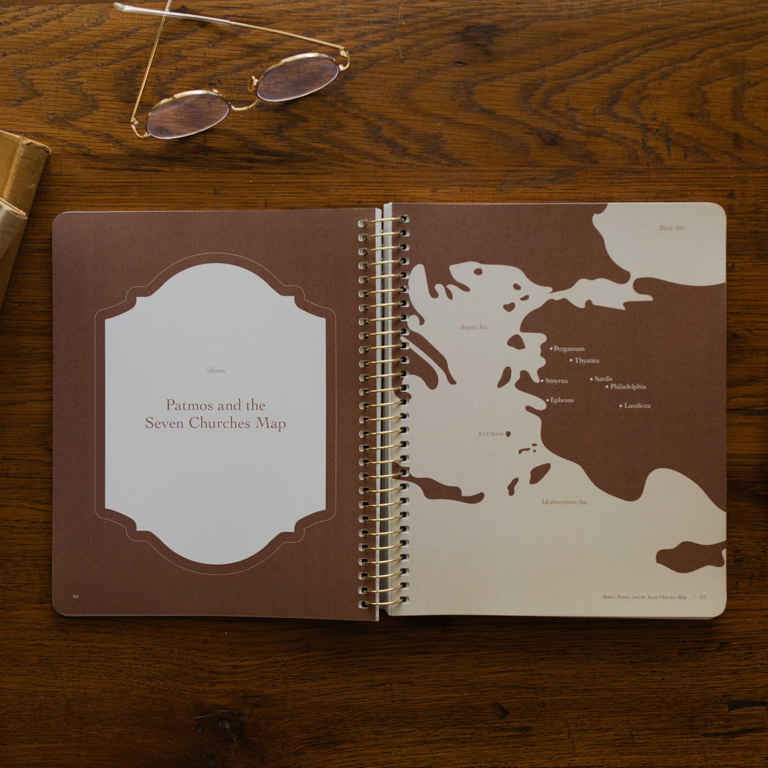 Revelation Spiral Study opened to page 64, Patmos and the seven churches map, on a wooden table next to a pair of glasses