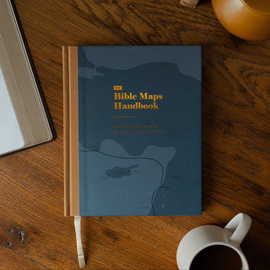 The Bible Maps Handbook cover on a wooden table near an open bible and a coffee cup