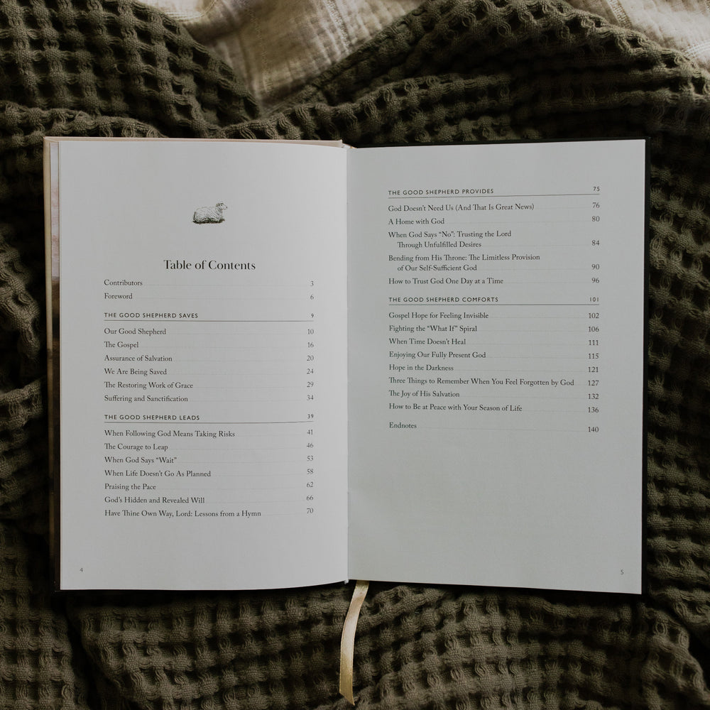 The Good Shepherd opened to the Table of Contents page laying on a green waffle styled blanket on another creme blanket