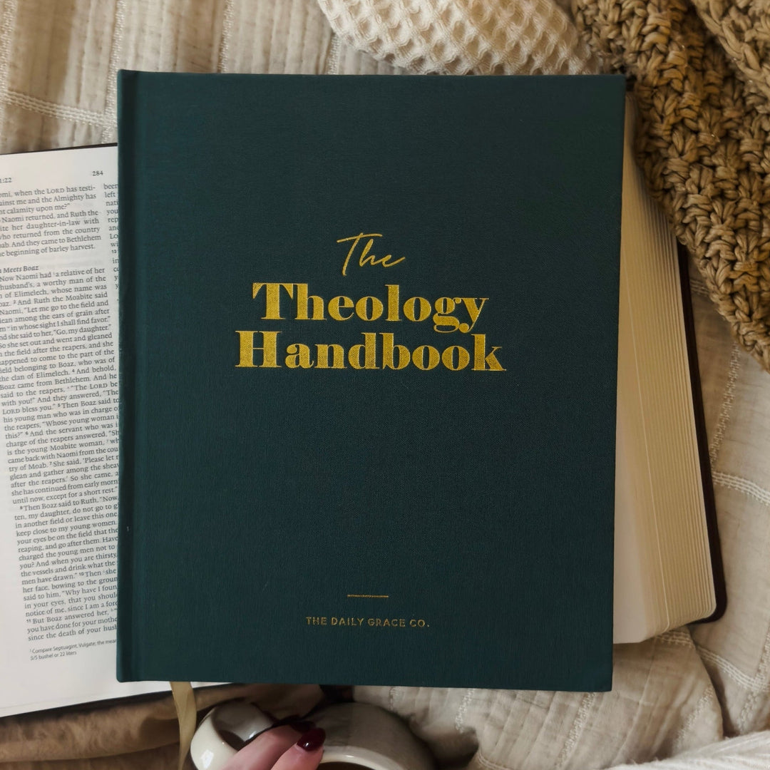 Theology Handbook with a hand holding a mug, surrounded by soft textures.